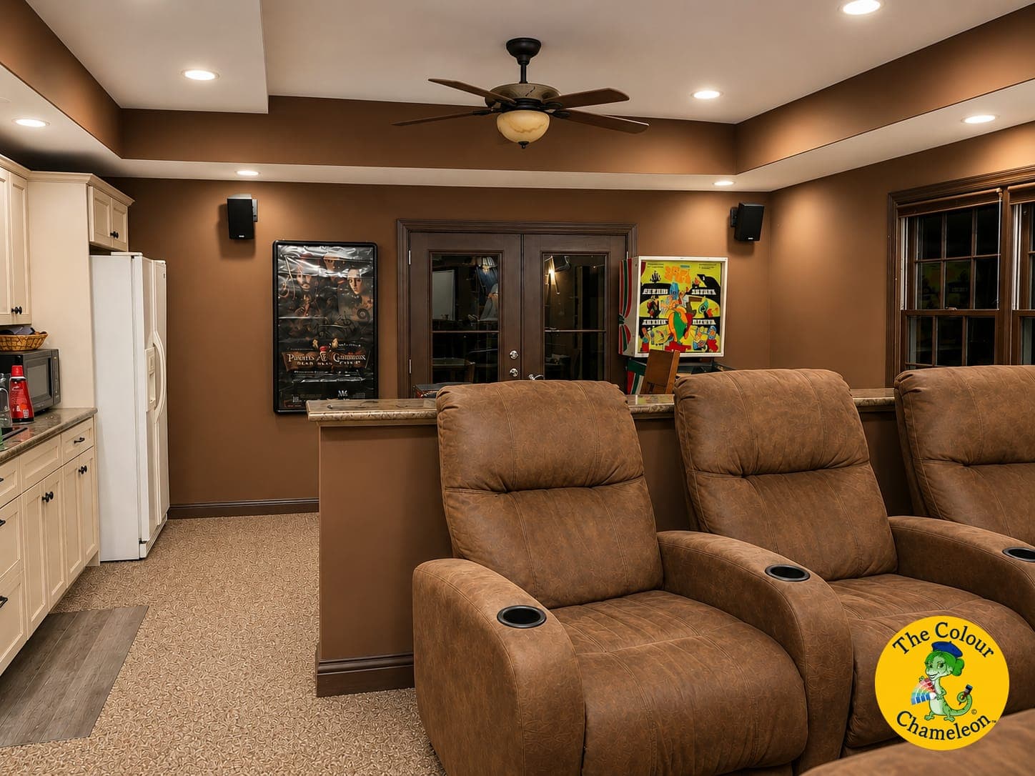 A finished basement with dark brown walls, beige carpet, cream cabinets and theater recliners