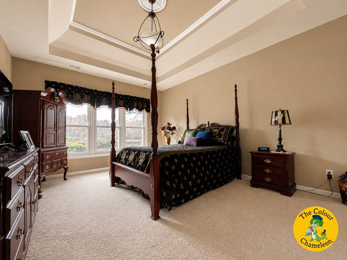 A bedroom with tan-yellow walls, a tray ceiling and a dark cherry four-poster bed