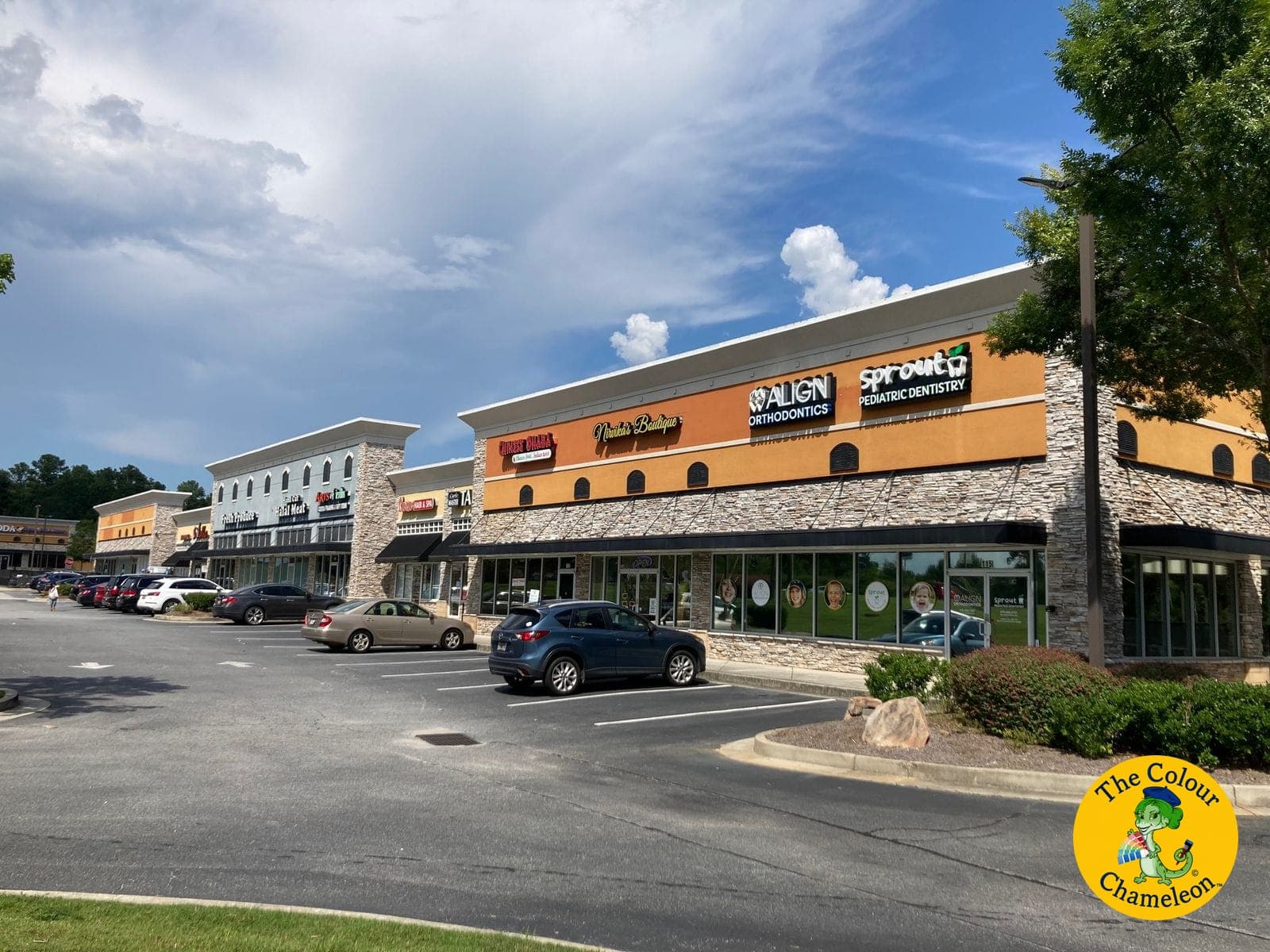 A retail shopping center with a bright orange painted band above the storefronts and stone columns