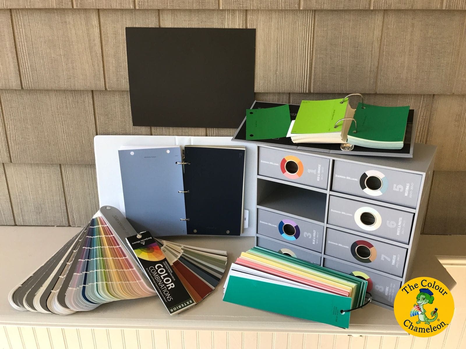Patricia's consultation kit laid out on a counter — fanned paint decks, ring-bound swatch binders, loose color strips and a set of labelled sample drawers