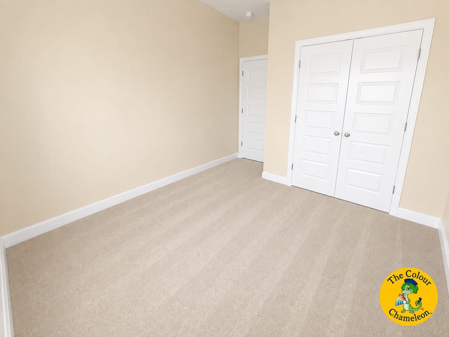 An empty room with builder-beige walls, beige carpet and white double closet doors