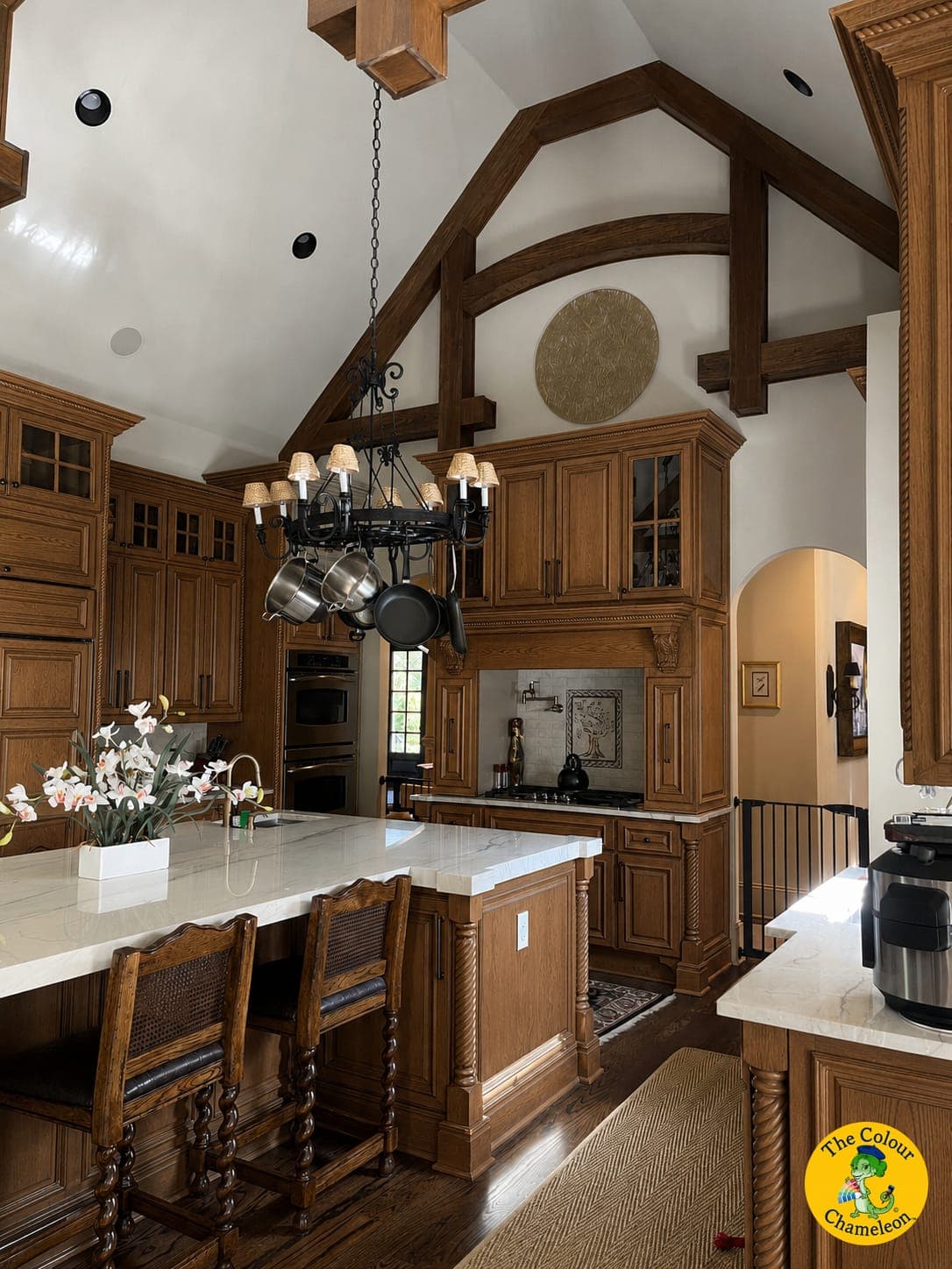 A vaulted kitchen with heavy stained-oak cabinetry, dark ceiling beams and an iron chandelier