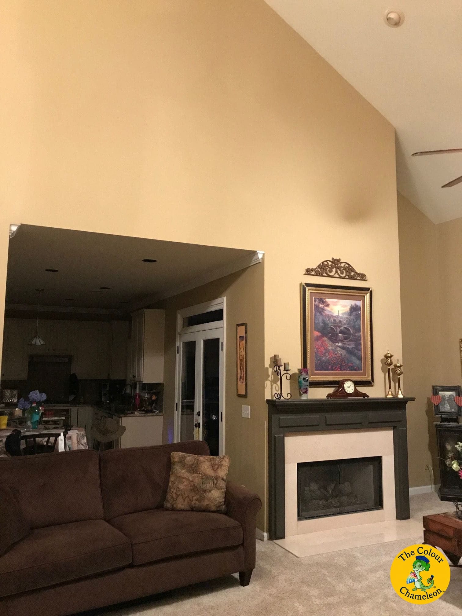 A vaulted living room with golden butterscotch walls, a dark mantel and a brown sofa